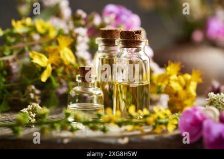 Bottiglie di olio essenziale aromaterapico con fiori estivi colorati su un tavolo Foto Stock