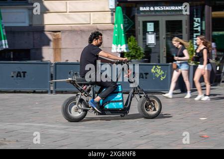 Corriere alimentare Wolt che guida ciclomotore elettrico nella zona pedonale di Aleksanterinkatu nel quartiere Kluuvi di Helsinki, Finlandia Foto Stock