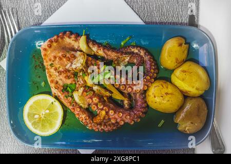 Polpo grigliato con salsa all'aglio e all'olio d'oliva, servito con patate, primo piano su un piatto Foto Stock