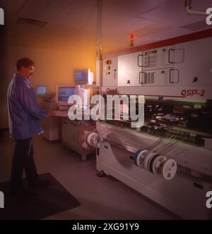 Tecnico che utilizza una macchina SMT automatizzata in laboratorio di produzione elettronica, che monitora la linea di produzione e le apparecchiature tramite interfaccia computer Foto Stock