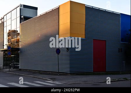 Questa immagine mostra un moderno edificio industriale con rivestimenti in metallo ondulato caratterizzati da vibranti pannelli gialli e rossi, che catturano l'essenza del contemporaneo Foto Stock