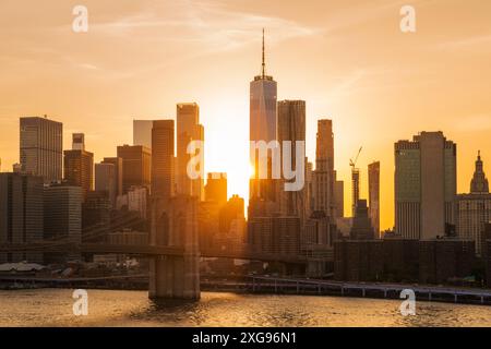 Ponte di Brooklyn e skyline di New York sull'East River illuminato da un intenso e ardente tramonto. I colori drammatici del cielo si riflettono sul Foto Stock