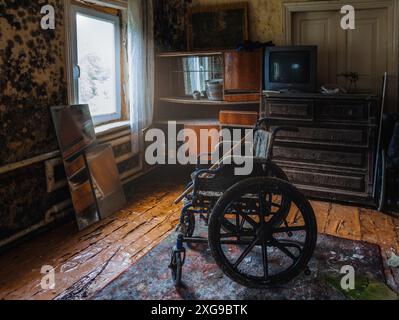 Sedia a rotelle vuota in una vecchia casa abbandonata. Foto Stock
