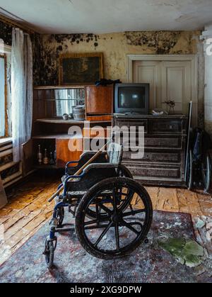 Sedia a rotelle vuota in una vecchia casa abbandonata. Foto Stock