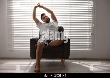 Uomo seduto su una poltrona vicino alle tendine della finestra all'interno Foto Stock