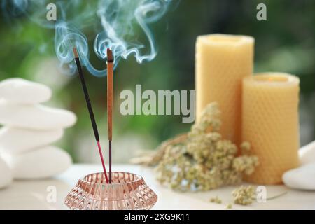 Bastoncini di incenso che si mescolano nel supporto vicino a pietre, candele e fiori secchi sul tavolo all'aperto Foto Stock