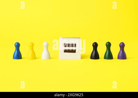 Pezzi di gioco di colori diversi e segno di uguale su sfondo giallo Foto Stock