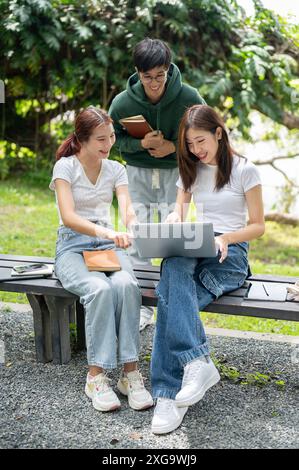 Un gruppo di giovani studenti universitari asiatici felici sta discutendo il loro progetto insieme, condividendo le loro idee, usando un portatile, lavorando insieme al banco i Foto Stock