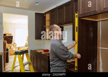 Durante l'installazione di un nuovo armadietto da cucina, il lavoratore rimane in piano per garantire che gli armadi siano in piano Foto Stock