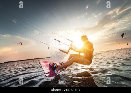 Una donna professionista di kite surfer cavalca su una tavola con un asse tra le mani su un lago leman con acqua di mare al tramonto. Spruzzi d'acqua e riflessi solari. Foto Stock