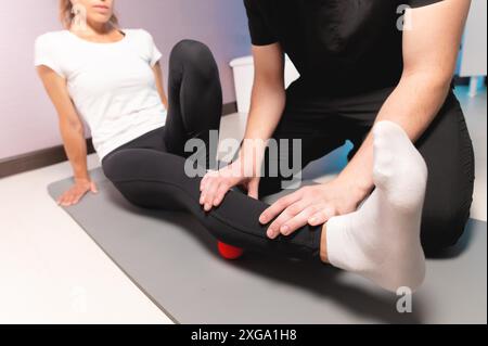 Il fisioterapista insegna l'auto-massaggio con palline rosse, paziente con lesioni alle gambe. Trattamento delle lesioni sportive. Uso pratico. Concetto di riabilitazione Foto Stock