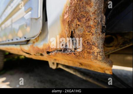 Interventi di riparazione e saldatura della carrozzeria richiesti. Ruggine su una vecchia macchina grigia. Foro di ruggine su una vecchia superficie metallica verniciata usurata Foto Stock