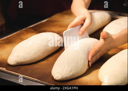 Una pagnotta cruda di pane francese si trova su un asse di legno. Preparazione prima della cottura del pane artigianale Foto Stock