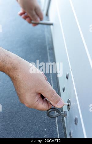 Primo piano di una mano con una chiave che chiude lo sportello dell'otturatore a rullo di un negozio. Concetto di chiusura Foto Stock
