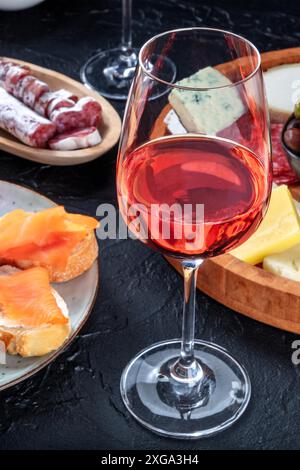 Un bicchiere di vino rosato con panini al salmone, formaggio e salumi. Tapas spagnole in un bar. Un primo piano di un drink a una festa Foto Stock