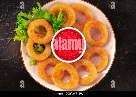 Anelli Calamari primo piano su nero. Squid anelli con foglie verdi di insalata e un tuffo, top shot su uno sfondo scuro Foto Stock