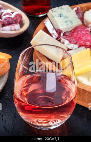 Vino rosato con prosciutto e formaggio. Tapas spagnole in un bar. Condivisione di cibo. Spuntini mediterranei su sfondo nero. Formaggio blu, salame e fuet Foto Stock