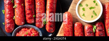 Salsicce alla griglia con ketchup e salsa di senape panorama su sfondo scuro. Frankfurter bratwurst, pasto tedesco Foto Stock