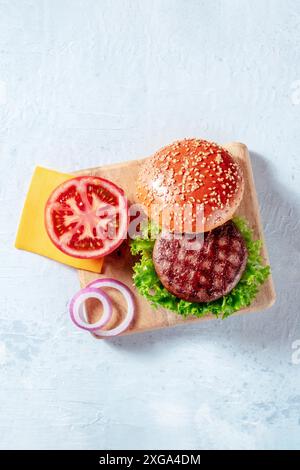 Ingredienti di hamburger, sparati dall'alto con un posto per il testo. Hamburger di manzo, pomodoro, formaggio, cipolla, insalata a foglia e pane di sesamo Foto Stock