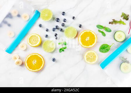 Sacchetti per la conservazione degli alimenti con frutta fresca estiva e verdure, sparati dall'alto su un tavolo da cucina in marmo bianco. Insalata estiva in contenitori con chiusura a zip Foto Stock
