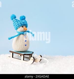 Piccolo pupazzo di neve lavorato a maglia in cappello blu e sciarpa. Buon Natale e biglietto di auguri di Capodanno 2025 Foto Stock