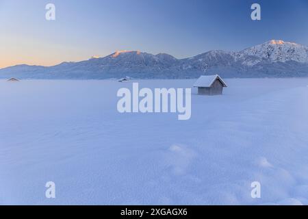 Capanna in legno al tramonto di fronte alle montagne, inverno, Loisach-Kochelsee-Moor, vista su Rabenkopf e Jochberg, Baviera, Germania, Europa Foto Stock