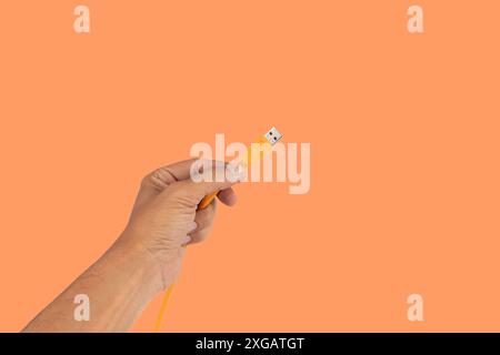 Mano maschio con cavo usb arancione isolato su sfondo arancione Foto Stock
