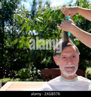 Un uomo anziano si fa tagliare i capelli all'aperto. Foto Stock