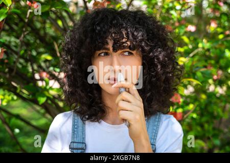 Giovane donna dai capelli scuri che usa spray nasale mentre ha sintomi di allergia Foto Stock