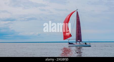 Barca a vela sulle piccole onde del mare aperto. Bandiera del paesaggio nautico con barca a vela - barca a vela a vela a vela a vela con spinnaker rosso che partecipa Foto Stock