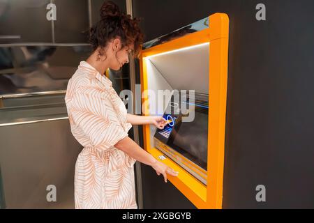 Donna latina ispanica che usa il bancomat durante il giorno. Vista laterale. Foto Stock