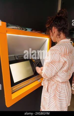 Donna latina ispanica che usa il bancomat durante il giorno. Vista posteriore. Foto Stock