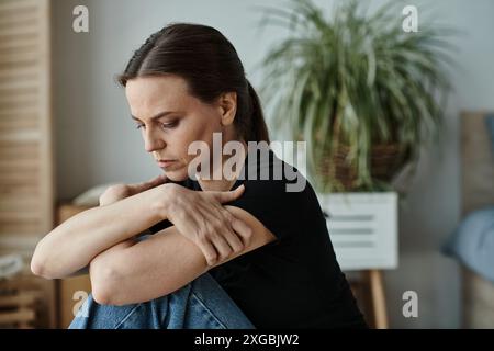 Donna di mezza età seduta sul pavimento, mani sulle ginocchia in profonda riflessione. Foto Stock