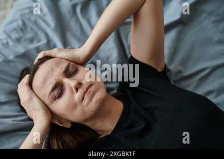 Donna di mezza età sdraiata a letto, mani appoggiate sulla testa, contemplando. Foto Stock