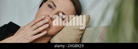 Una donna di mezza età sdraiata con la mano sul viso, profondamente nel pensiero. Foto Stock