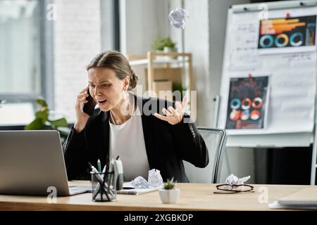 Donna di mezza età che parla al telefono alla scrivania dell'ufficio, sopraffatta dallo stress. Foto Stock