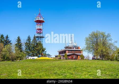 Questa immagine mostra la Torre di osservazione Kozakov nel Paradiso boemo, Cechia, in una giornata di sole. La torre si erge su di un cielo azzurro e in primo piano si trova un edificio con un tetto rosso. Foto Stock