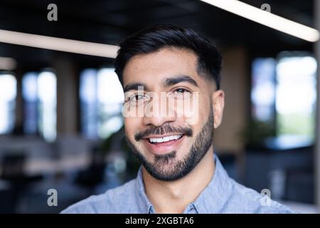 Sorridente in ufficio, uomo d'affari che indossa una camicia blu, sicuro di sé e professionale Foto Stock