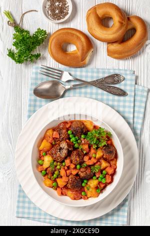 stufato turco di polpette, sulu kofte, piatto abbondante con patate, carote e piselli verdi sospesi in salsa di pomodoro servito in un recipiente con forchetta e cucchiaio su w. Foto Stock