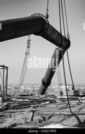 Un colpo verticale in scala di grigi di un enorme tubo sollevato da catene pesanti in un cantiere di Johannesburg, Sudafrica Foto Stock