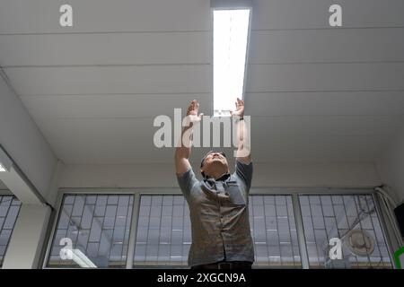 Lampadina a risparmio energetico per scatti ad angolo elevato in una lampada bianca sul soffitto, che controlla o sostituisce le luci fluorescenti negli edifici. Uomo felice che cambia a l Foto Stock