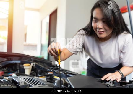 Donna sorridente che controlla l'olio motore dell'auto controlla l'olio motore dell'auto in ambienti chiusi. Una donna si sta occupando di un'auto in casa sua, pronta ad andare al lavoro. Foto Stock
