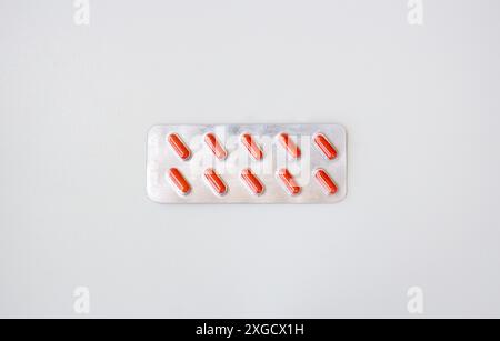 Capsule mediche rosse confezionate in blister isolato su sfondo bianco. Striscione orizzontale con spazio per la copia. Farmacia, trattamento, concetto di problema di salute Foto Stock