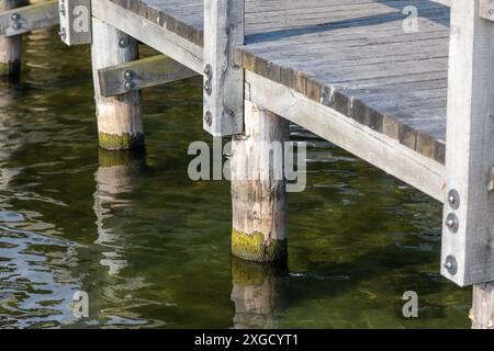 Un molo o molo in legno si estende sulle acque calme del lago, con i supporti in legno visibili sotto la superficie. Foto Stock