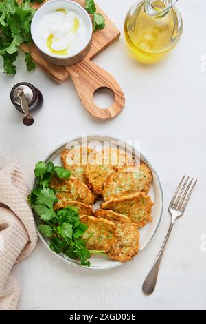 Frittelle di zucchine vegetali con panna acida pepe e olio d'oliva servite su un piatto rustico su un vecchio sfondo di piastrelle incrinate. Vegetariano sano per Foto Stock