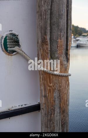 Una barca bianca è legata a un molo di legno (delfino) con una corda spessa. Foto Stock