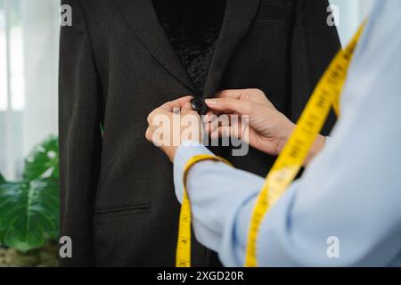 Primo piano di un abito sartoriale su un modello maschile, mani con metro a nastro, giacca di fissaggio a spillo su un modello maschile. Vestito semilavorato su manichino Foto Stock