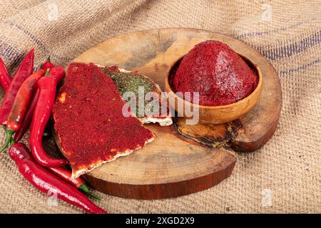 Pasta di peperoncino su fondo di legno. Pasta di peperoni alla turca (biber salcasi). Recipiente in legno con salsa rossa e peperoncino fresco. Foto Stock