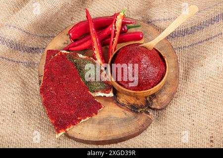 Pasta di peperoncino su fondo di legno. Pasta di peperoni alla turca (biber salcasi). Recipiente in legno con salsa rossa e peperoncino fresco. Foto Stock