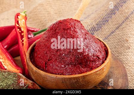 Pasta di peperoncino su fondo di legno. Pasta di peperoni alla turca (biber salcasi). Recipiente in legno con salsa rossa e peperoncino fresco. Foto Stock